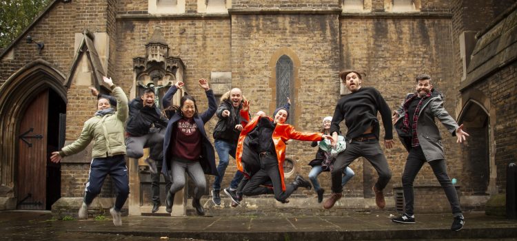 A group of happy young people, jumping in the air, outside Holy Cross Church on Cromer Street